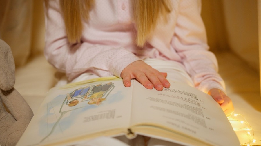 Una bambina in pigiama sfoglia un libro di fiabe tra le lucine