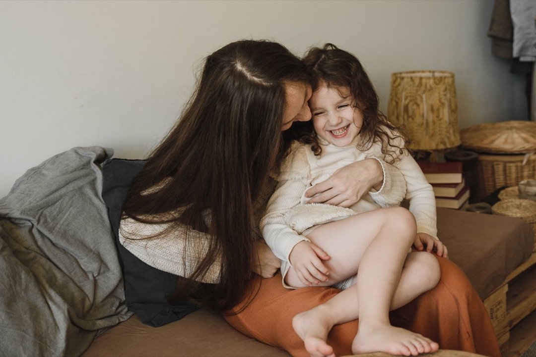 Una madre e una bambina ridono abbracciate sul divano